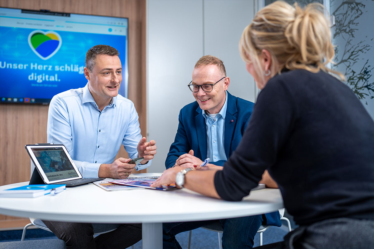 Besprechung zu dritt vor einem Bildschirm mit dem Digitalclaim des Medienhauses