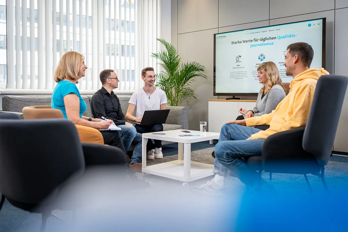 Mitarbeitende der Freien Presse Mediengruppe im Gespräch in der Loungezone vor einer Präsentationswand
