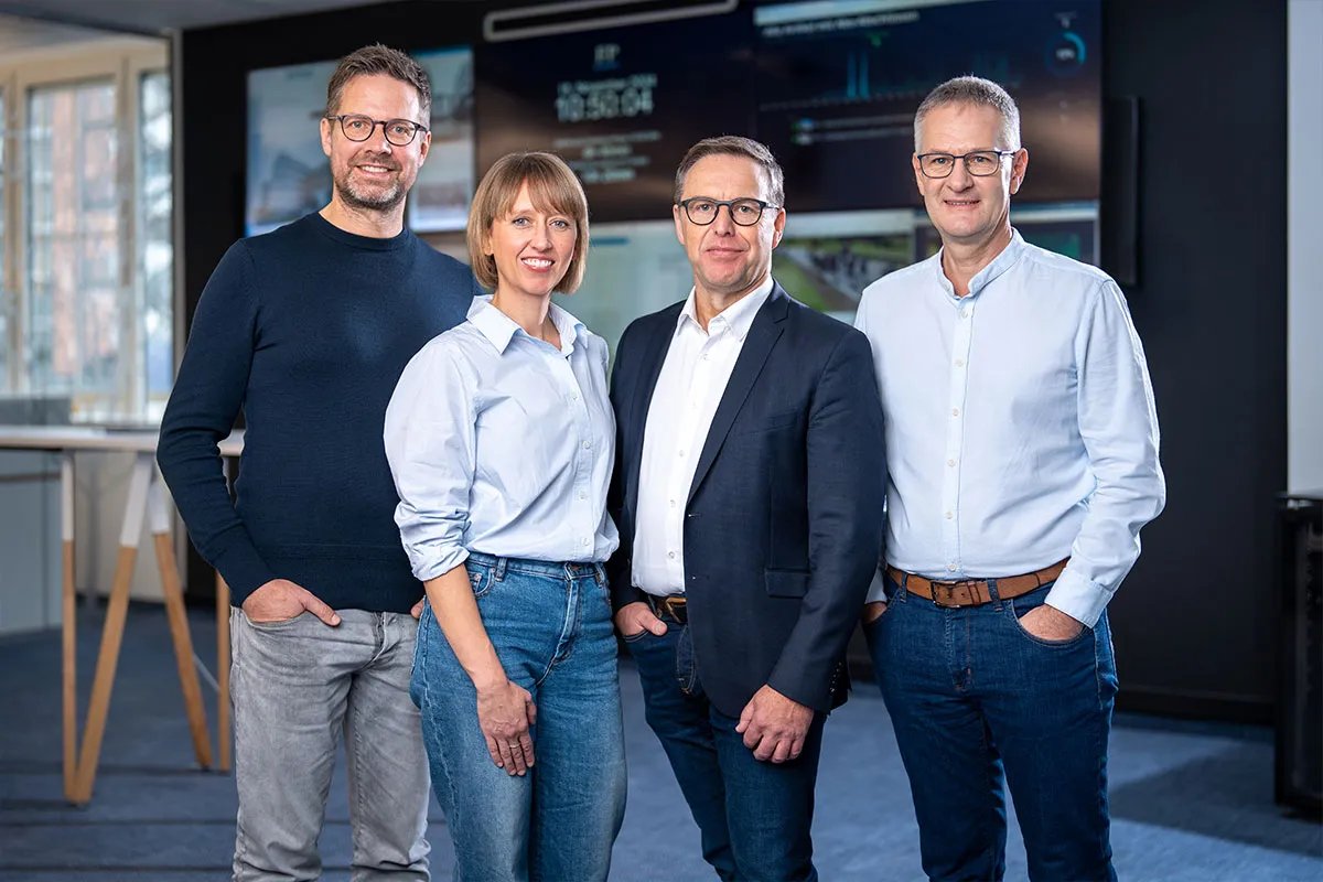 Vierköpfiges Team vor einer Bildschirmwand im Redaktionsbüro